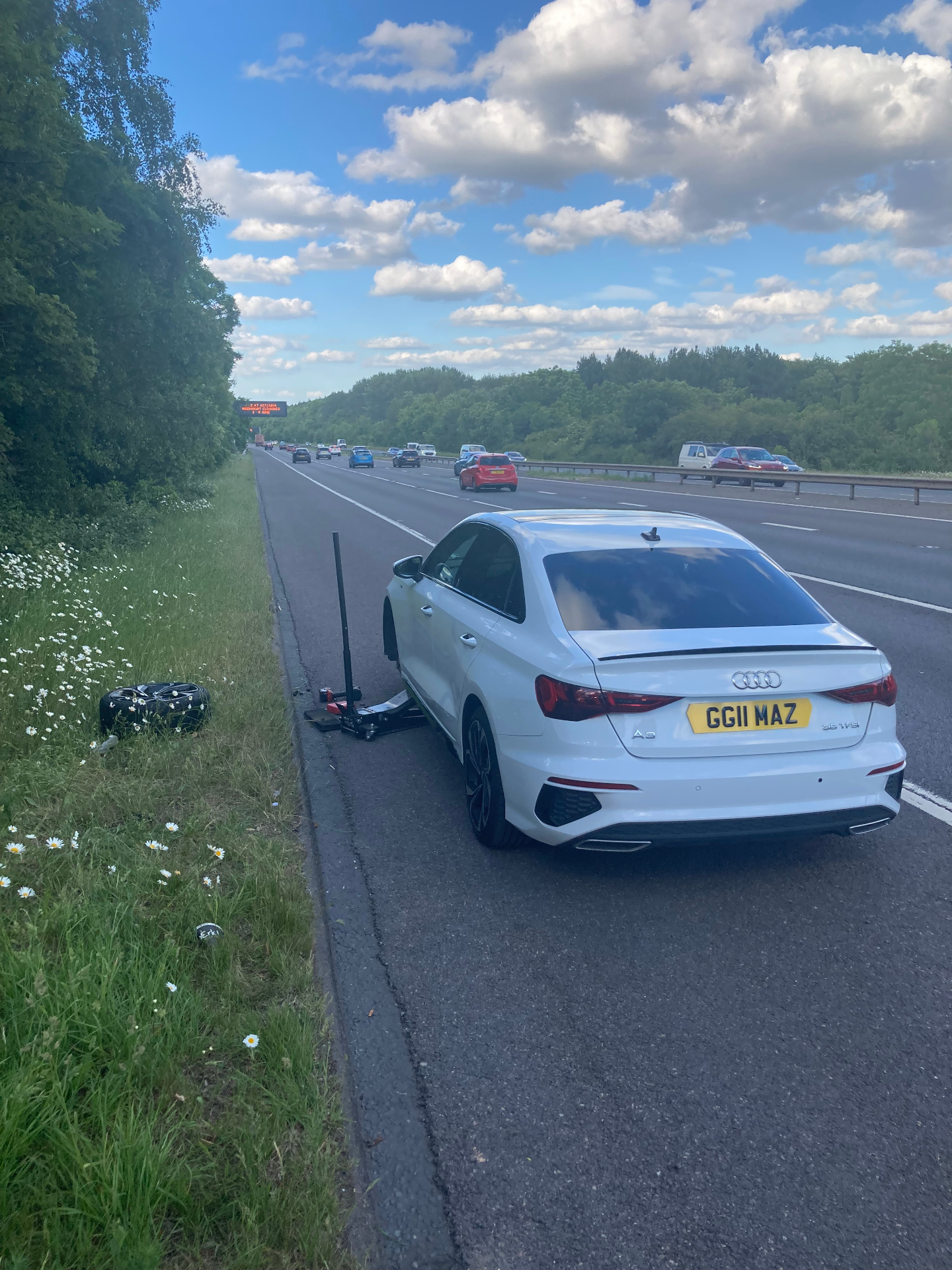 Emergency roadside tyre fitting on a white Audi A3 on the motorway hard shoulder